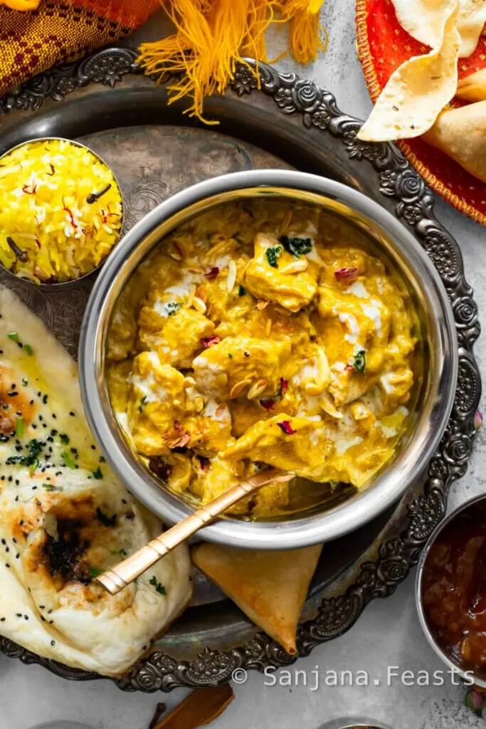 A bowl of vegan tofu korma with yellow colour next to naan bread