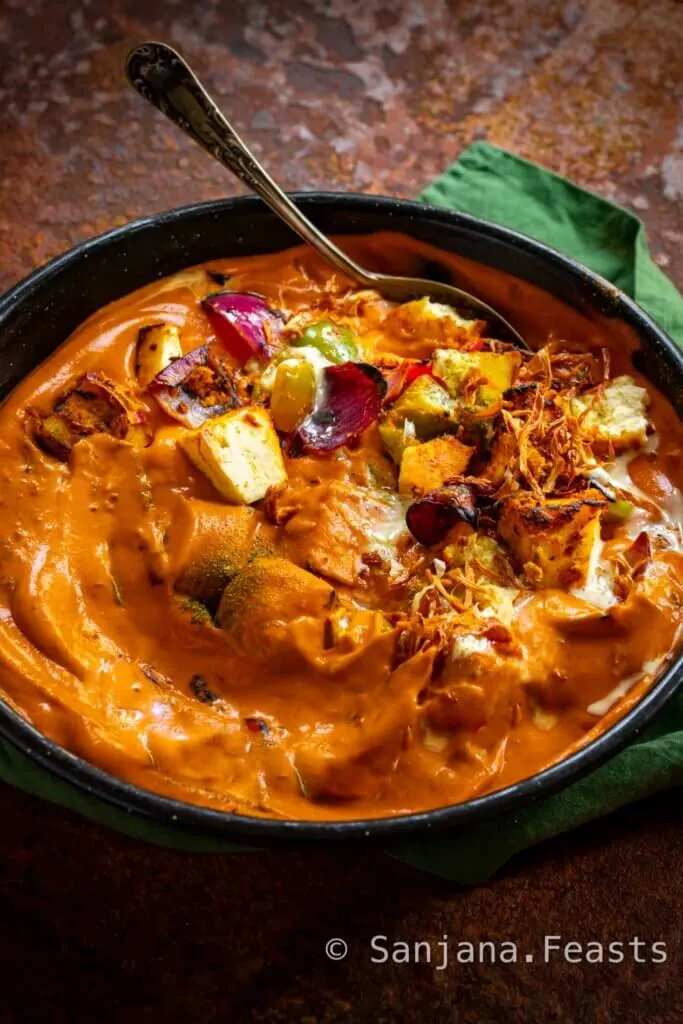 Bowl of paneer tikka masala with fried onion garnish and spoon