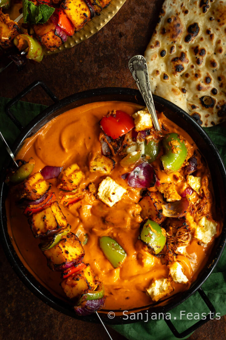 Paneer Tikka masala with skewer of grilled paneer tikka resting on the side of the bowl