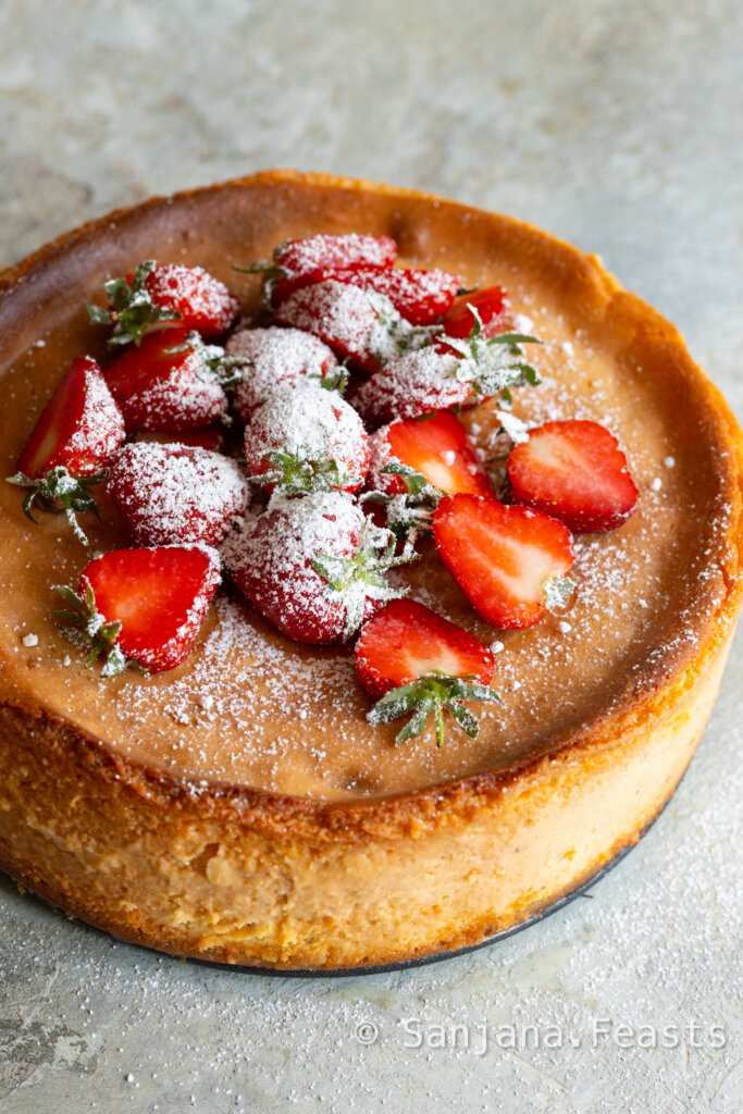 shrikhand cheesecake whole topped with strawberries and icing sugar